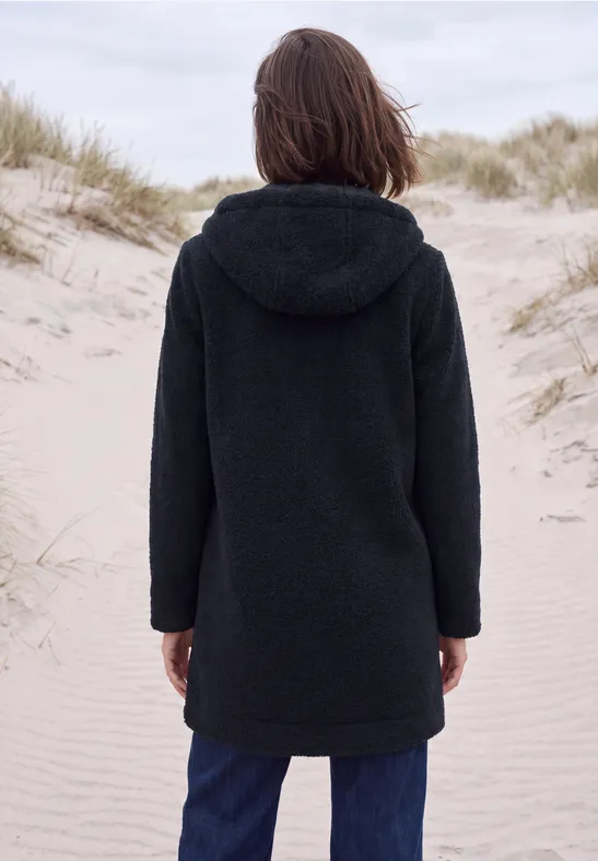Personne en manteau à capuche noir debout de dos sur des dunes de sable.