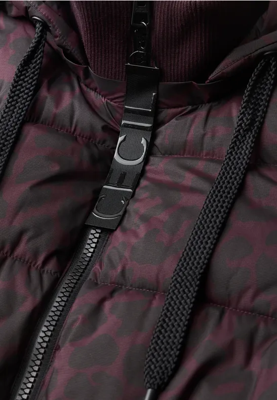 Close-up van een donkerrode gewatteerde jas met zwart ritssluiting, koord en metalen gesp.