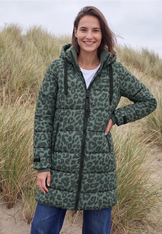 Vrouw in groene gewatteerde jas met luipaardprint, glimlachend voor duinen.