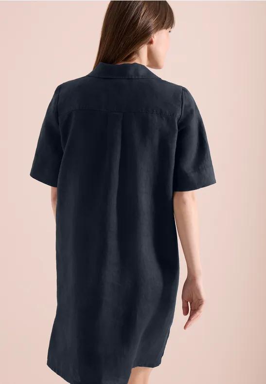 Rückenansicht einer Frau im kurzärmeligen, knielangen, dunklen Hemdkleid vor rosafarbenem Hintergrund.