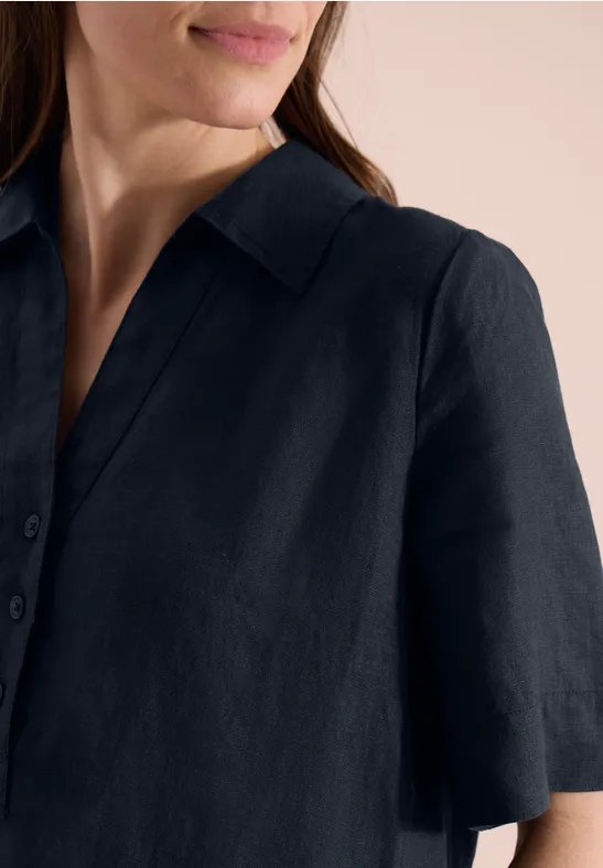 Eine Frau trägt ein dunkelblaues, kurzärmliges Leinenhemd mit Kragen.