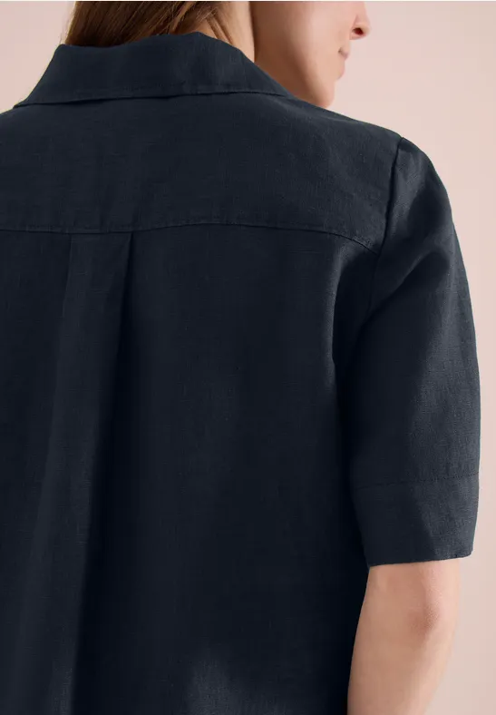 Rückansicht einer Person mit halblangem braunem Haar in schwarzem Leinenhemd mit Kurzarm.