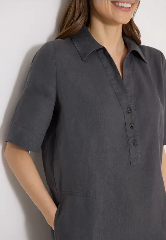 Eine Frau trägt ein dunkelgraues Kurzarm-Hemd mit Knopfleiste und seitlichen Eingrifftaschen.