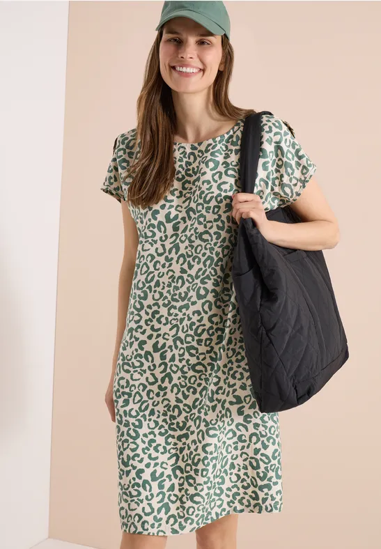 Frau in grünem Leopardenmuster-Kleid trägt große schwarze Tasche.