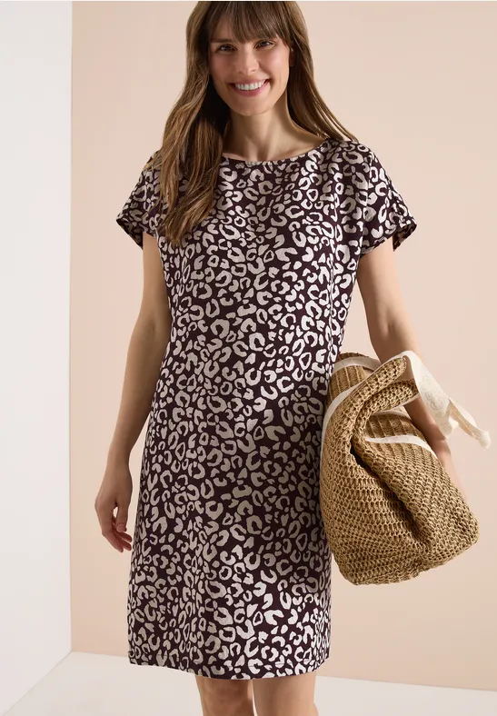 Frau trägt ein kurzärmliges, knielanges schwarz-weißes Leopardenkleid und hält eine geflochtene Strohtasche.