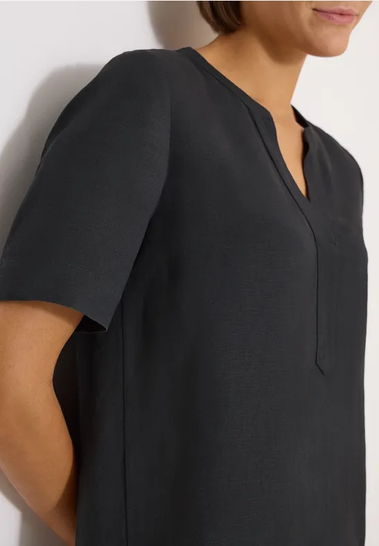 Nahe Aufnahme einer Frau in schwarzer Bluse mit kurzem Arm vor weißem Hintergrund.