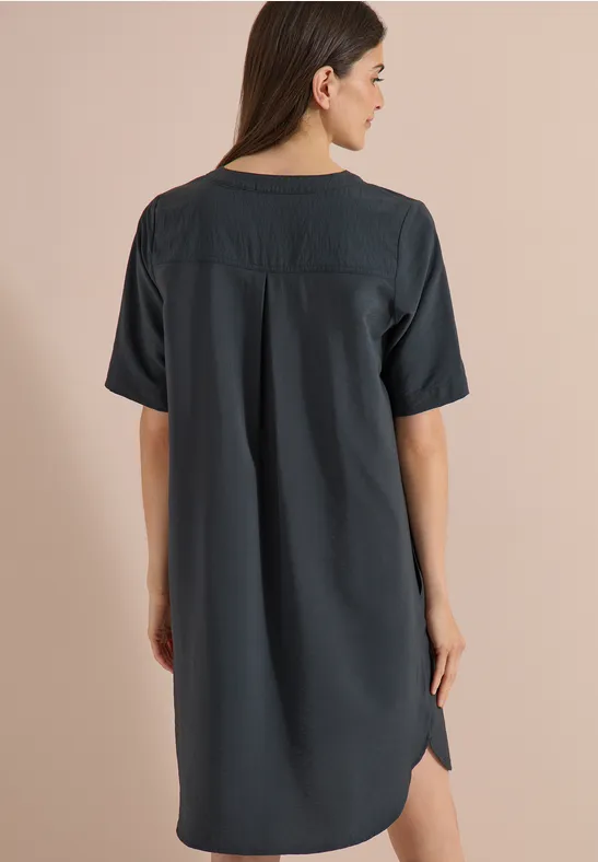 Frau von hinten in locker sitzendem, knielangem, dunklem Kleid mit kurzen Ärmeln und Rückendetail.