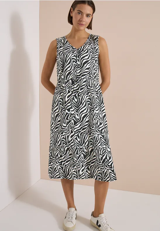 Femme porte une robe midi sans manches à motif zèbre, associée à des baskets blanches.
