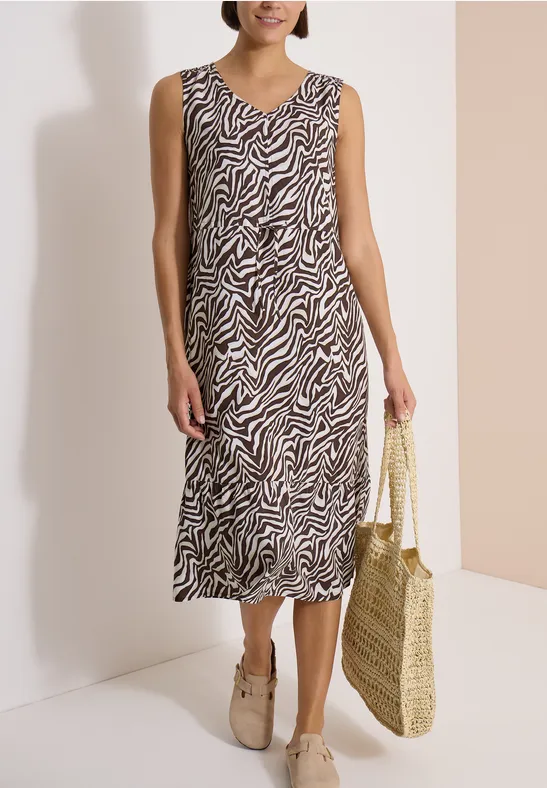 Femme en robe midi sans manches à motif zèbre, sac en osier et mocassins beiges.