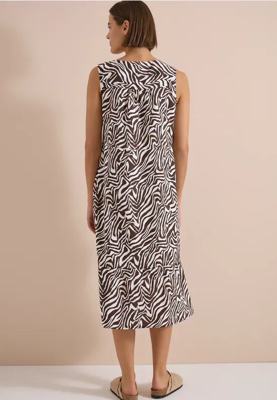 Femme vue de dos, robe midi sans manches à motif zèbre, chaussures plates.