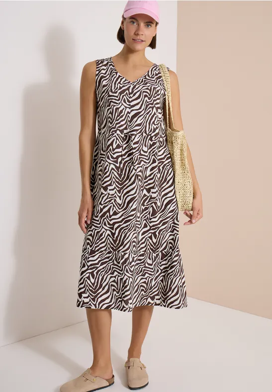 Femme porte une robe midi sans manches à motif zèbre et un sac jaune.