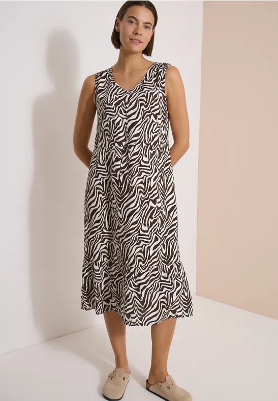 Femme en robe midi sans manches à motif zébré et mocassins beiges sur fond neutre.