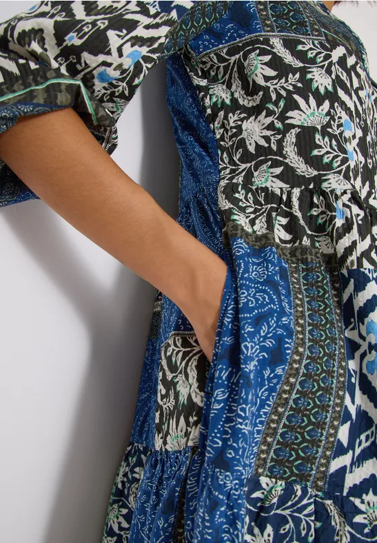 Hand in Seitentasche eines langen Kleides mit blauem, weißem und schwarzem Patchwork-Print.