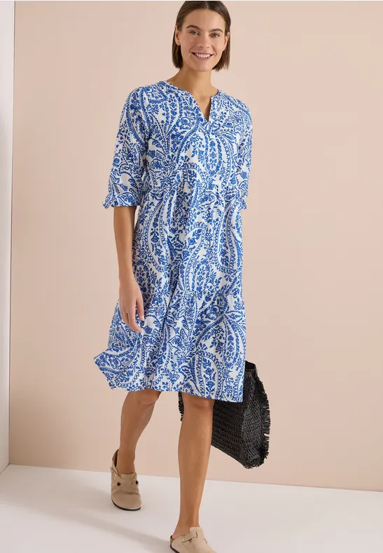 Dame in blau-weiß gemustertem Midikleid mit V-Ausschnitt, halblangen Ärmeln und Plattform-Sandalen.