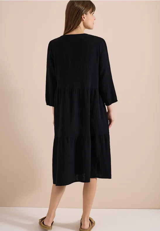 Frau von hinten in einem knielangen, schwarzen Stufenkleid mit 3/4-Ärmeln.