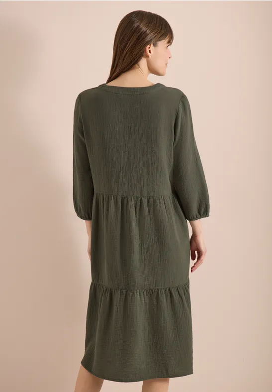 Frau von hinten in locker sitzendem, olivegrünem, stufigem Midi-Kleid mit 3/4-Ärmeln.