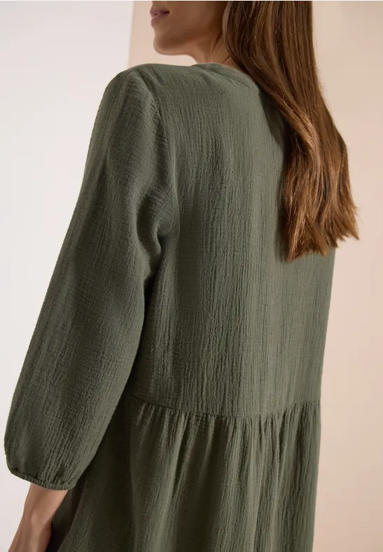 Frau von hinten in locker sitzendem, olivgrünem Kleid mit geraffter Taille.