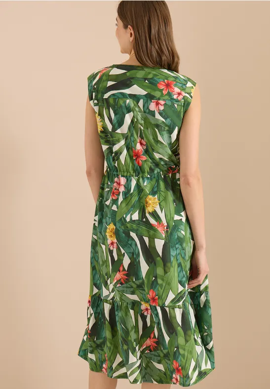 Frau von hinten in grünem, ärmellosem Kleid mit tropischem Blatt- und Blumenmuster.