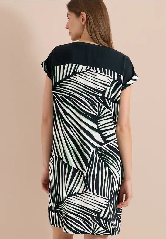Frau von hinten in lockerem Kurzarm-Kleid mit schwarzem Oberteil und grün-weißem Blätterprint.