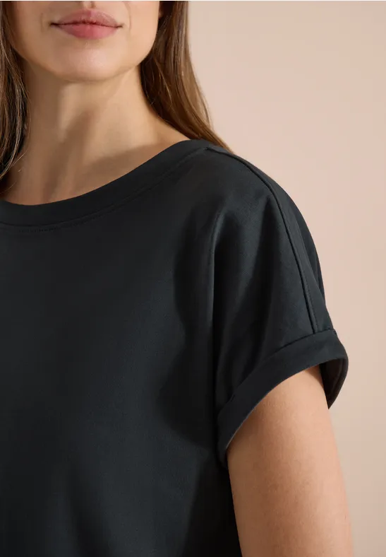 Nahaufnahme eines weiblichen Oberkörpers in schlichtem schwarzem T-Shirt mit kurz umgeschlagenen Ärmeln.