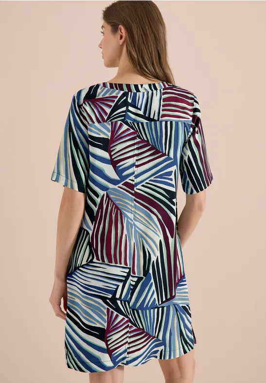 Vrouw van achteren in korte jurk met korte mouwen en abstract streepmotief in blauw, paars en wit.