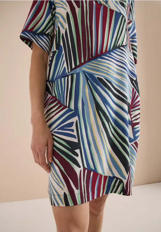 Gedeeltelijke weergave van een persoon in een kleurrijke jurk met abstract geometrisch patroon.