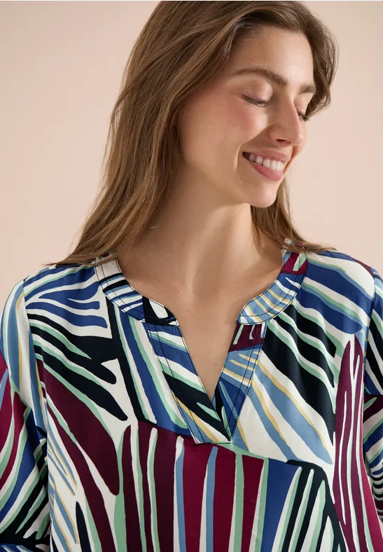 Vrouw draagt een blouse met abstracte, meerkleurige strepenpatroon.