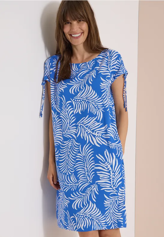Eine Frau trägt ein knielanges hellblaues Kleid mit weißen Blattmustern und kurzen Ärmeln.