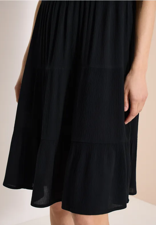 Schwarzes, knielanges Stufenkleid aus leichtem Stoff.