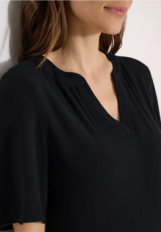 Schlichte, schwarze Damenbluse mit V-Ausschnitt und kurzen Ärmeln, nah am Oberkörper.