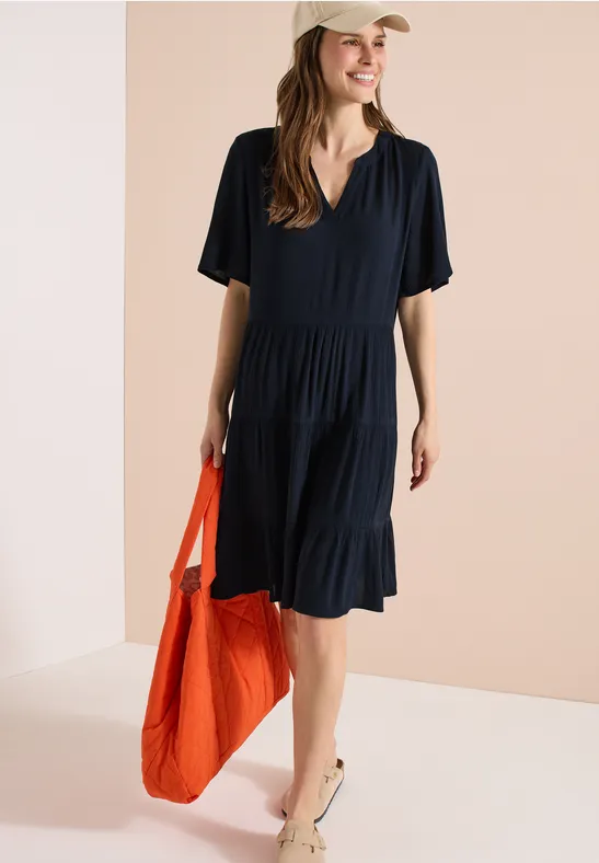 Frau in lockerem, schwarzem Kleid mit V-Ausschnitt trägt orangefarbene Tasche.