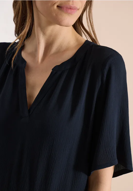 Eine Frau trägt eine schwarze, leicht strukturierte V-Ausschnitt-Bluse mit kurzen Ärmeln.