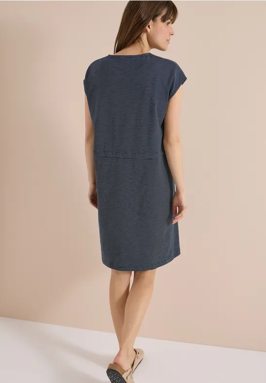 Rückansicht einer Frau in kurzem Jeanskleid und flachen Sandalen.