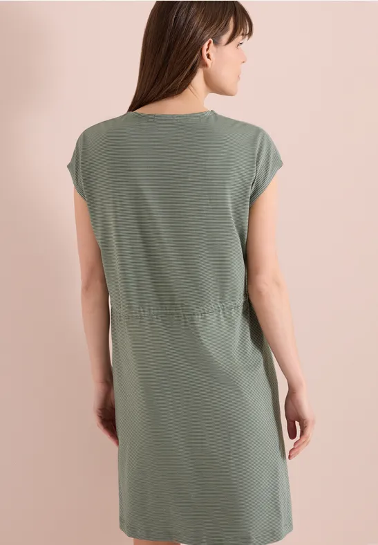 Frau steht mit dem Rücken zur Kamera, trägt grünes kurzärmeliges knielanges Kleid.