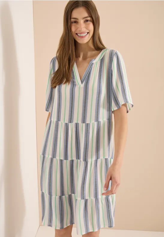 Dame im gestreiften V-Neck Midi-Kleid mit Stufenrock und kurzen Ärmeln vor hellem Hintergrund.
