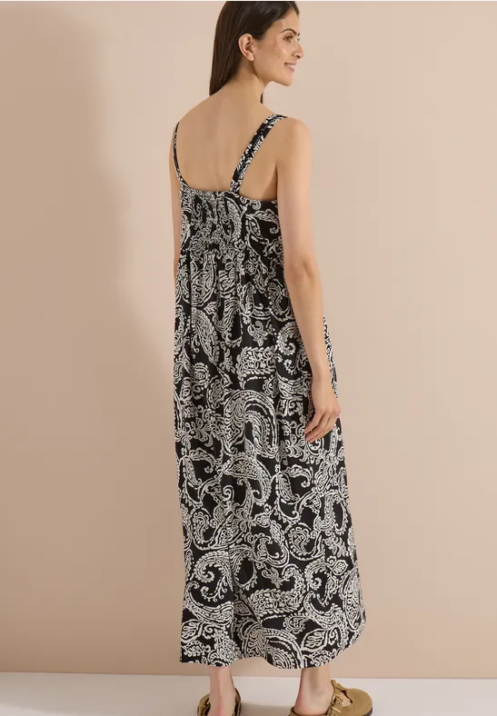 Femme de dos portant une robe longue noir et blanc à imprimé cachemire avec fines bretelles.