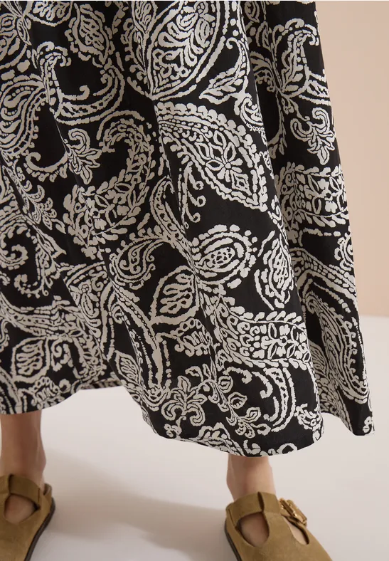 Maxi-jupe noire à motif cachemire blanc portée avec des sandales marron.