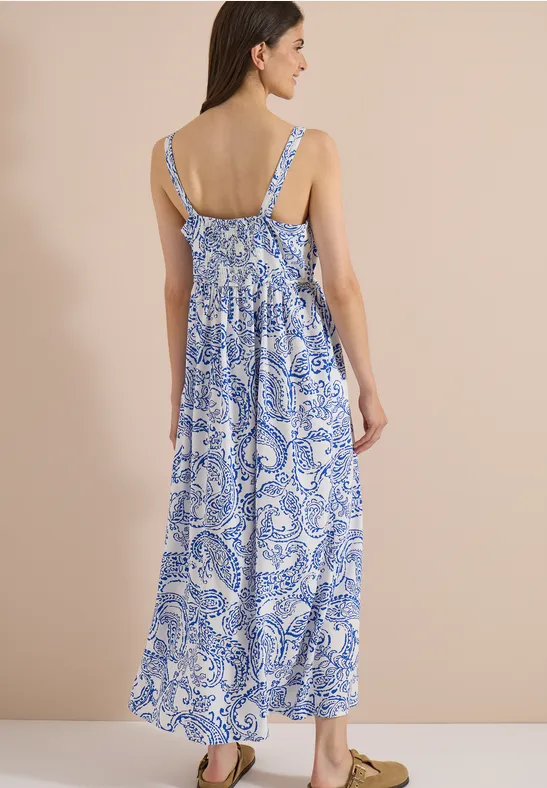 Femme vue de dos portant une longue robe maxi bleu et blanc à fines bretelles, motif cachemire.