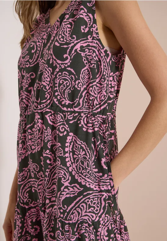 Een vrouw draagt een mouwloze jurk met roze paisleyprint op een donkere stof.