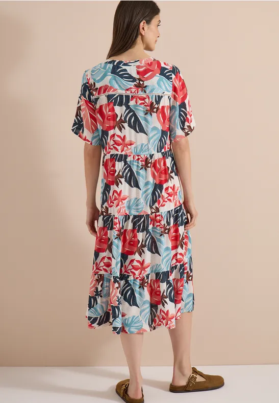 Vue arrière d’une femme portant une robe blanche mi-longue à imprimé floral coloré et manches amples sur fond neutre.