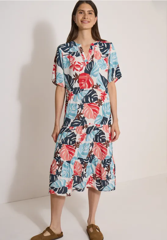 Une femme porte une robe midi colorée à motif de feuilles tropicales.