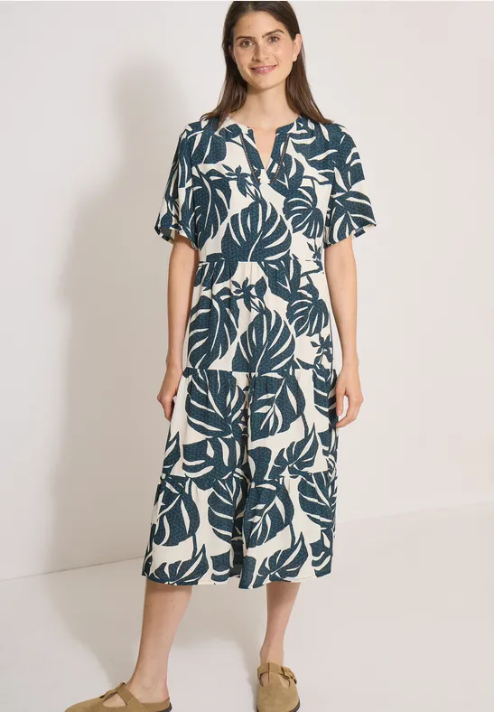 Frau in midi-weißem Hemdblusenkleid mit grünem Blattmuster, kurzärmelig, tailliert, Knopfleiste.
