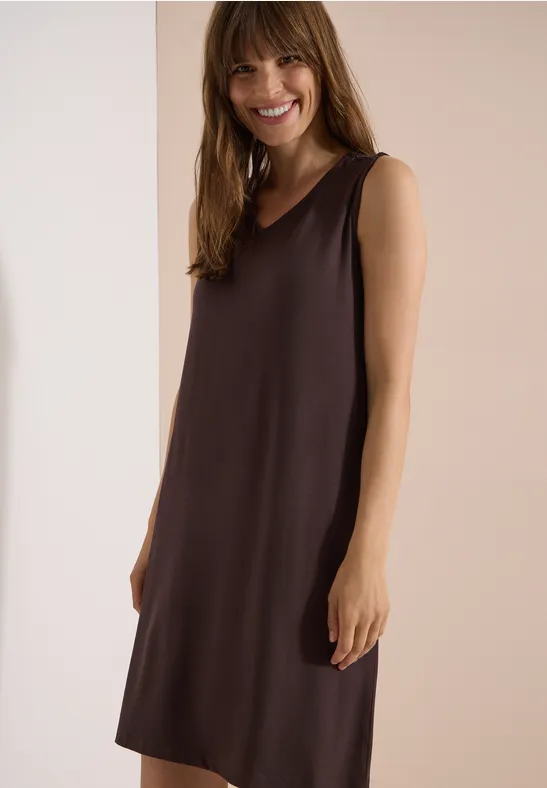 Frau trägt ärmelloses, knielanges, braunes Kleid mit schlichter Silhouette.