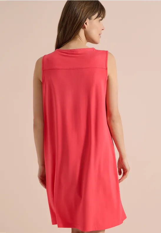 Eine Frau trägt ein ärmelloses rotes Kleid, Rückenansicht vor neutralem Hintergrund.