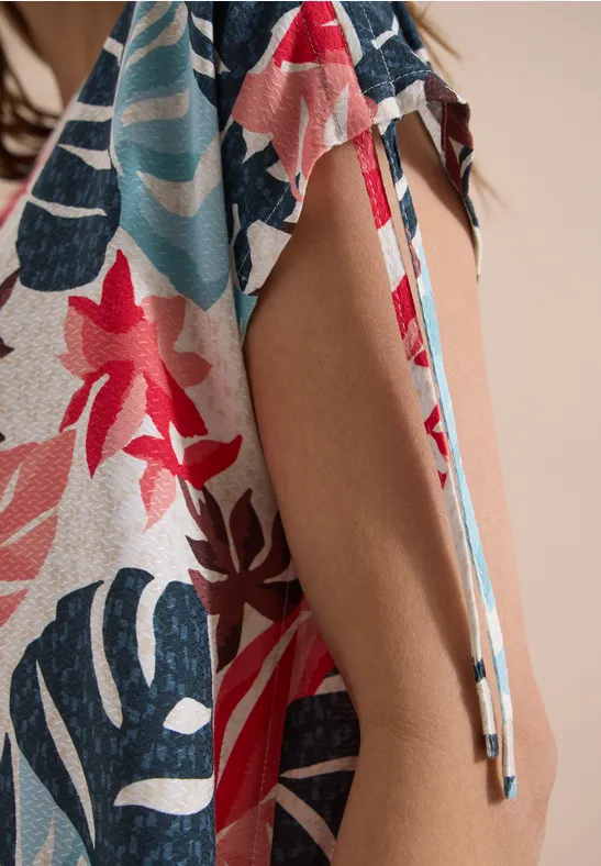 Close-up van lichte stof met kleurrijke bloemen- en bladerenprint, zijsplit met bindbandje.