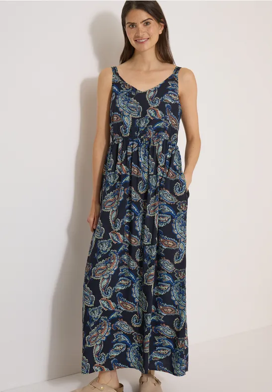 Frau trägt ärmelloses, bodenlanges Maxikleid mit Paisley-Muster in Blau- und Grüntönen.
