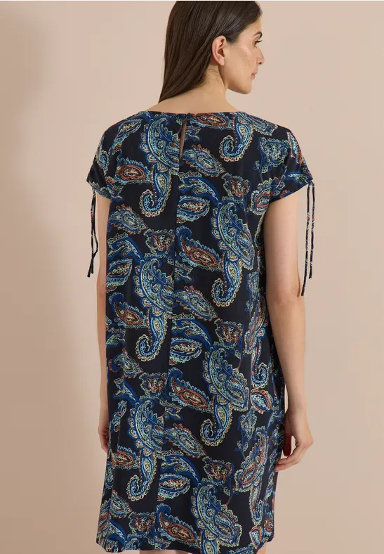 Femme vue de dos, portant une robe ample mi-longue à motif cachemire bleu et manches à liens.