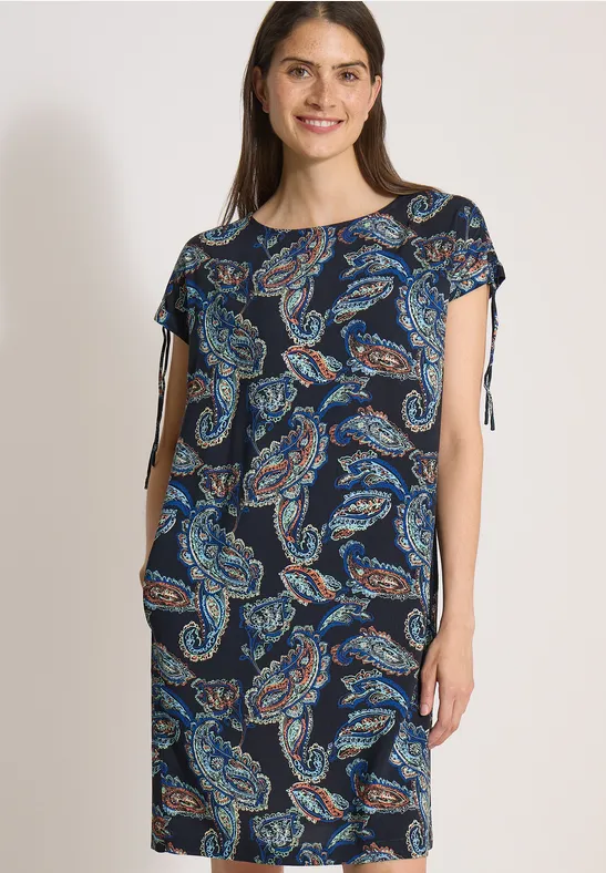 Femme portant une robe bleu marine à motifs cachemire, manches courtes et liens latéraux.