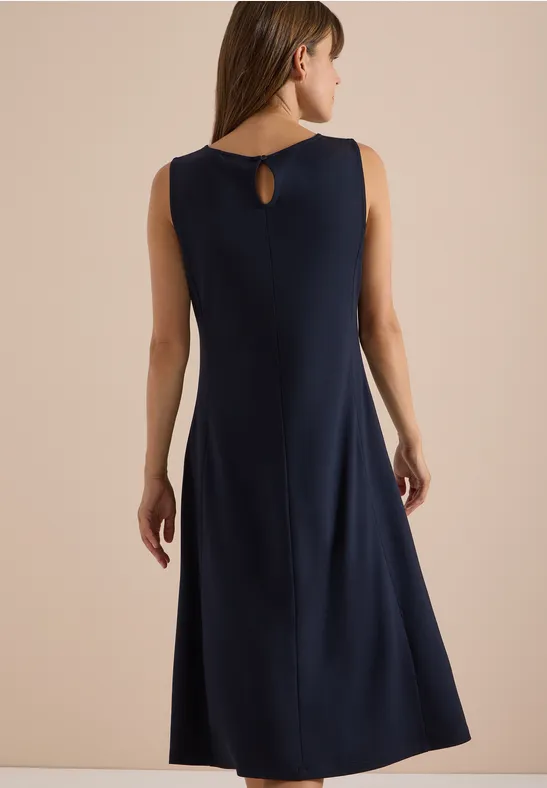 Vrouw van achter gefotografeerd in een donkerblauwe mouwloze midijurk met klein rugdetail en uitlopende rok.