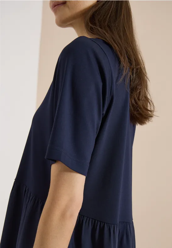 Frau in locker sitzendem dunkelblauem T-Shirt vor hellem Hintergrund